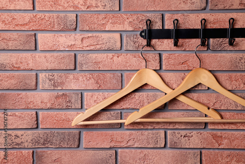 Hook rack with wooden clothes hangers on red brick wall. Space for text