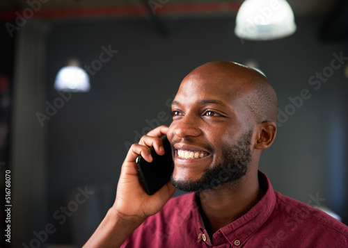 A Black man smiles on a cellphone call in the office