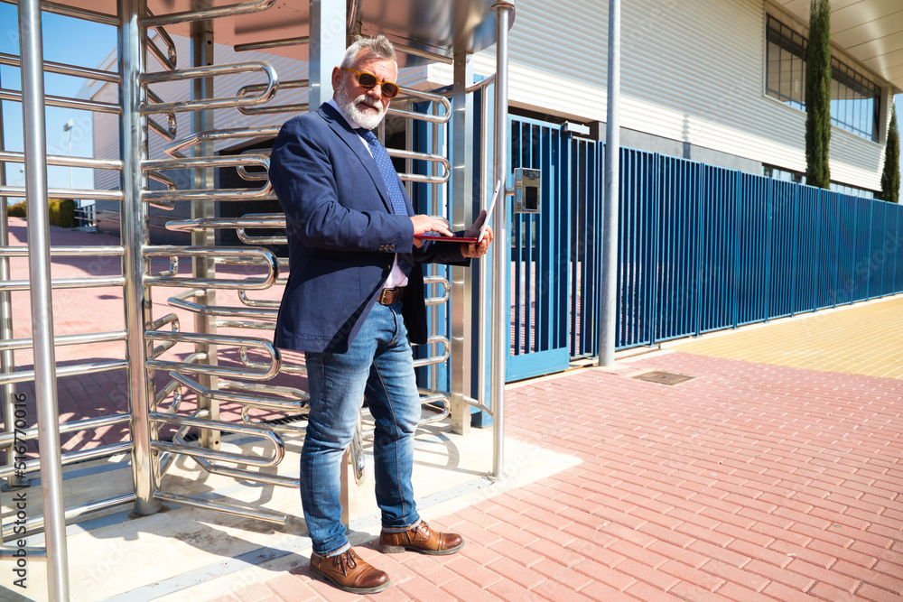 Mature professor, grey-haired, bearded, with sunglasses, is consulting his laptop before entering the university. Concept of education and teaching. Teachers and retirement.