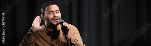 Quadro em tela indian comedian listening and performing stand up comedy into microphone on black with smoke, banner