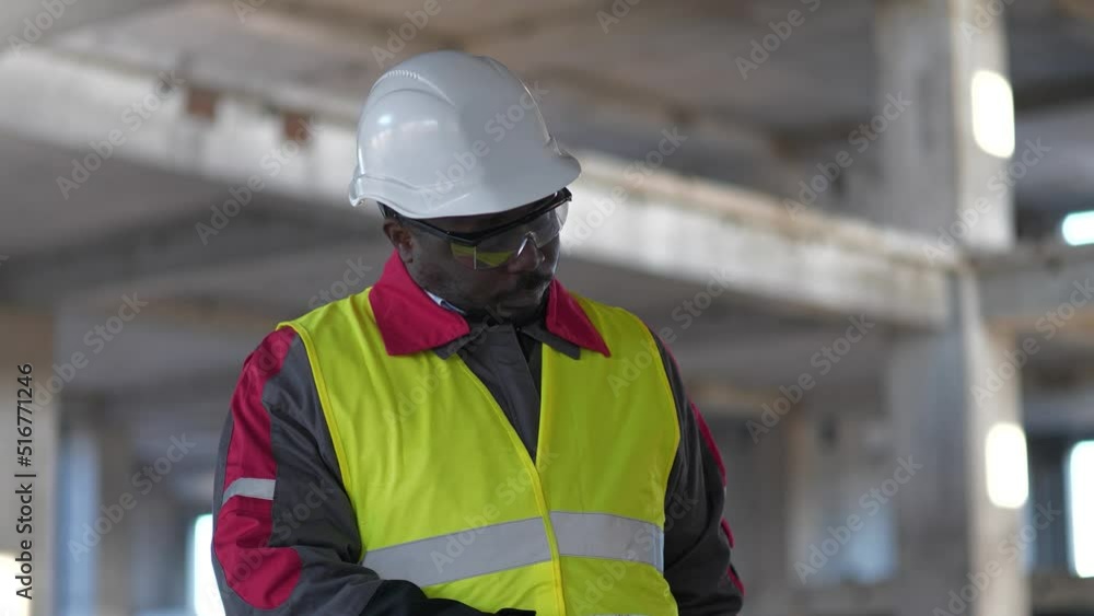 Slow Motion African american worker pulls phone out of pants, talks on smartphone at construction site. Builder in white hard hat speaks on smartphone at project site Slow Motion African american worker pulls phone out of pants, talks on smartphone at construction site. Builder in white hard hat speaks on smartphone at project site