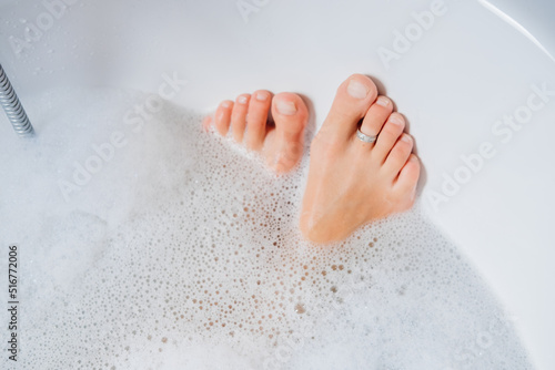 Self care. Young adult woman taking bath and lying in foam water. Female feet. Selective focus © Maria