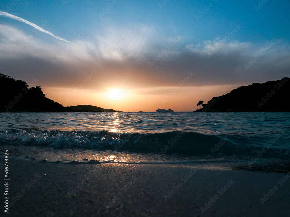 Obraz premium Sunset on a sandy beach with beautiful sea waves and little isles on background