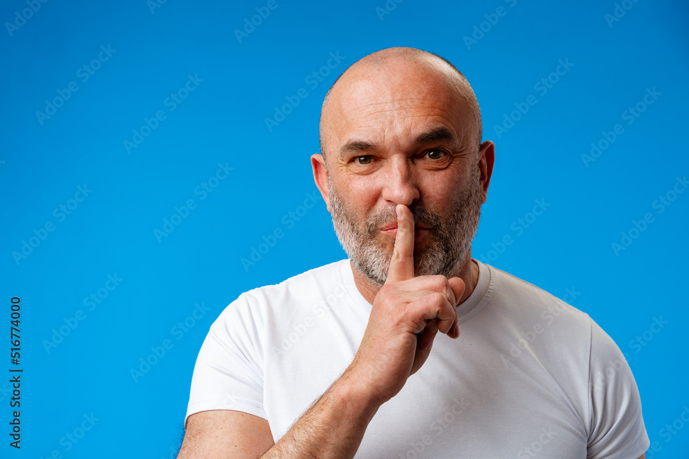 Middle age man wearing t-shirt over blue wall asking to be quiet Middle age man wearing t-shirt over blue wall asking to be quiet