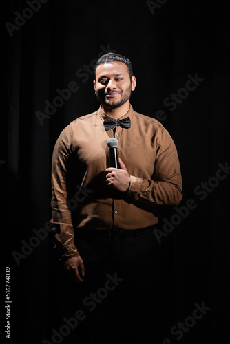 smiling middle east comedian performing stand up comedy into microphone on black.