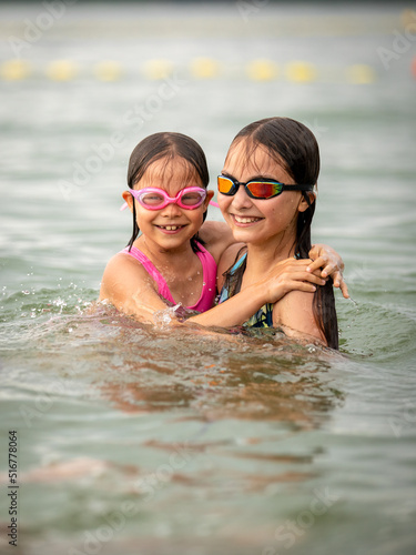 Girls sisters swimming together in water and smiling in summer