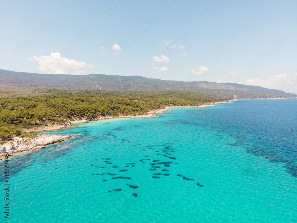 Aerial view of scenic and clear turquoise sea water from above  with white rocks and green trees around,  Mediterranean travel concept, Portokali beach in Sithonia, Greece 