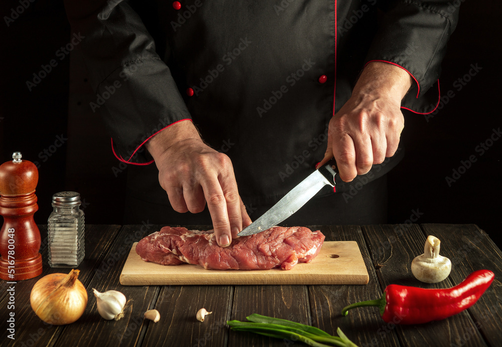 Experienced chef cuts raw beef meat on a cutting board before baking. Hotel menu recipe idea