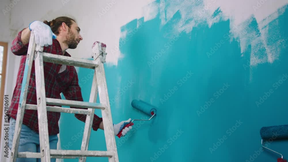 Charismatic Caucasian looking using the wall brush roller to paint the
