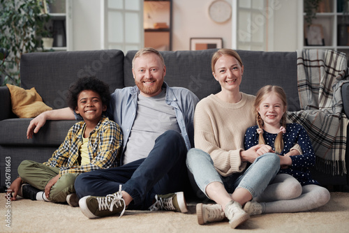 Portrait of happy family with adopted children sitting on floor in living room and smiling at camera photo