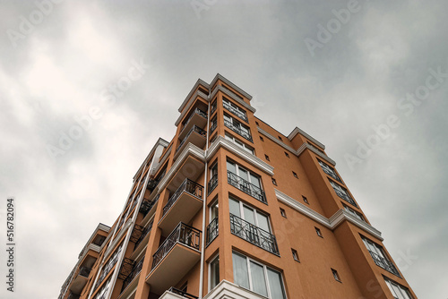 Street photography. Modern residential building with balconies in a residential complex. A yellow multi-storey building against a blue cloudy sky. A yellow house against the sky.
