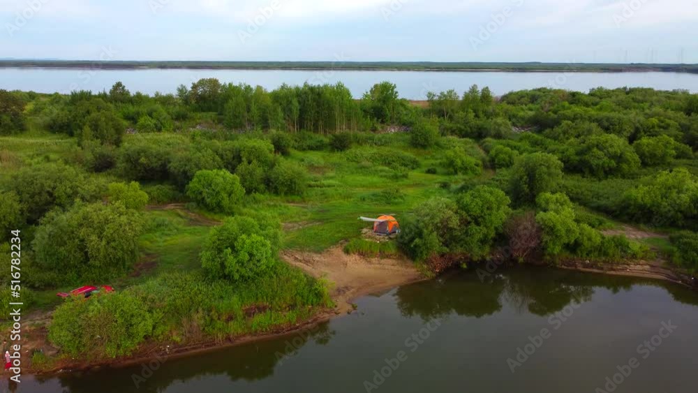 Lake at dawn before sunrise. There is a lonely camping tent on the shore. The Amur River is in the distance. The drone descends down over the surface of the water. Lake at dawn before sunrise. There is a lonely camping tent on the shore. The Amur River is in the distance. The drone descends down over the surface of the water.