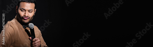 Photography skeptical indian stand up comedian telling joke into microphone and pouting lips isolated on black, banner