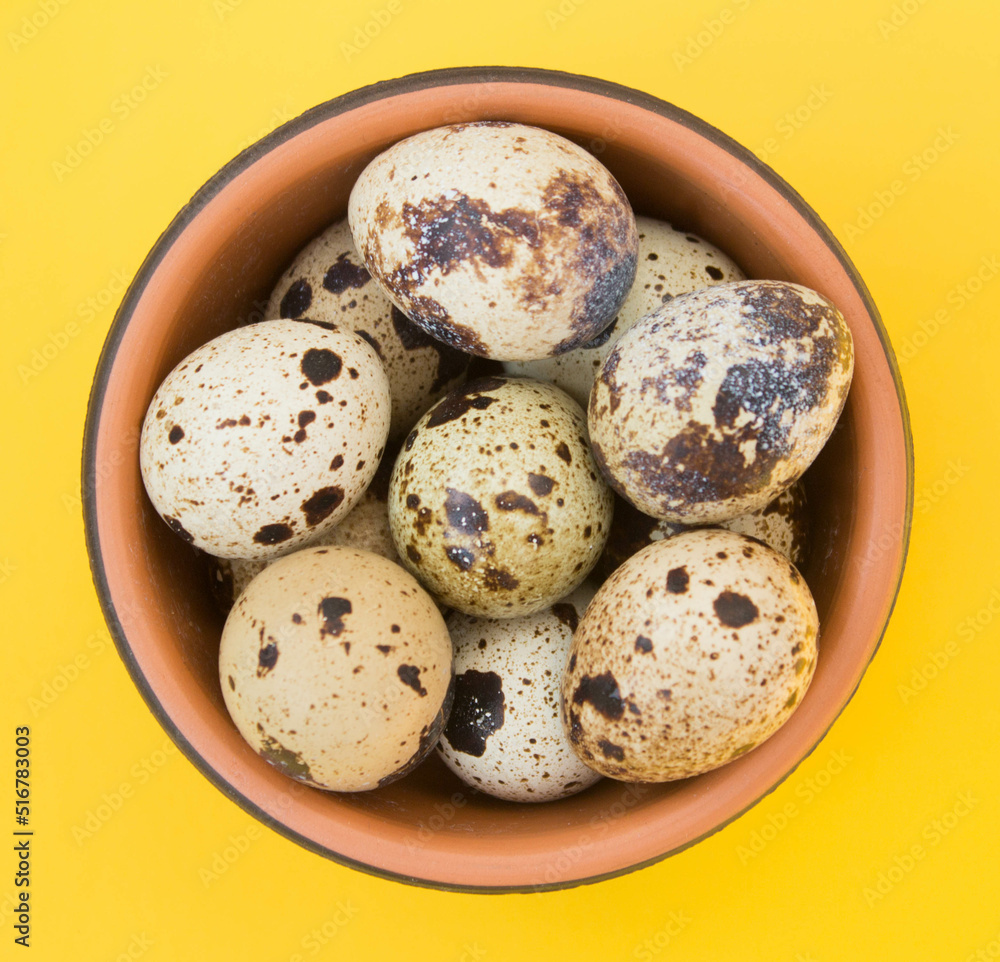 Raw fresh quail eggs in brown bowl. Top view. Yellow background. Raw fresh quail eggs in brown bowl. Top view. Yellow background.