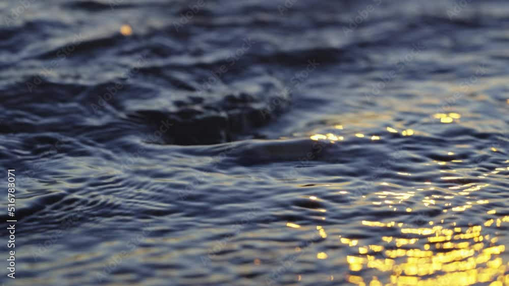 Close up of waves lapping against a singular peddle as the sun sets Close up of waves lapping against a singular peddle as the sun sets
