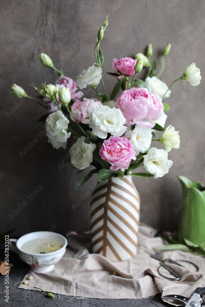 A beautiful bouquet of white lisianthus and pink peonies in a vase on a table with a linen napkin. Seasonal summer flowers. A beautiful bouquet of white lisianthus and pink peonies in a vase on a table with a linen napkin. Seasonal summer flowers.