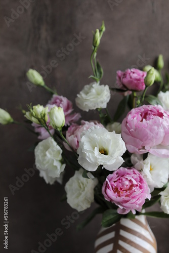 A beautiful bouquet of white lisianthus and pink peonies in a vase on a table with a linen napkin. Seasonal summer flowers.