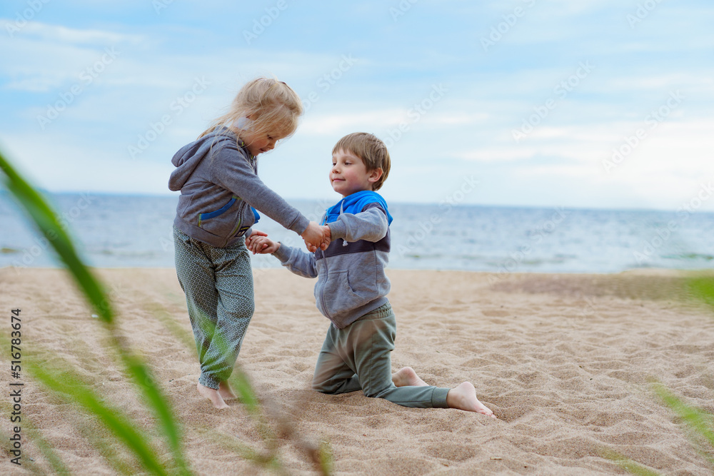 Brothers and little sister during summer vacations having fun on sandy beach.girl helping boy to stand up. Children support Brothers and little sister during summer vacations having fun on sandy beach.girl helping boy to stand up. Children support