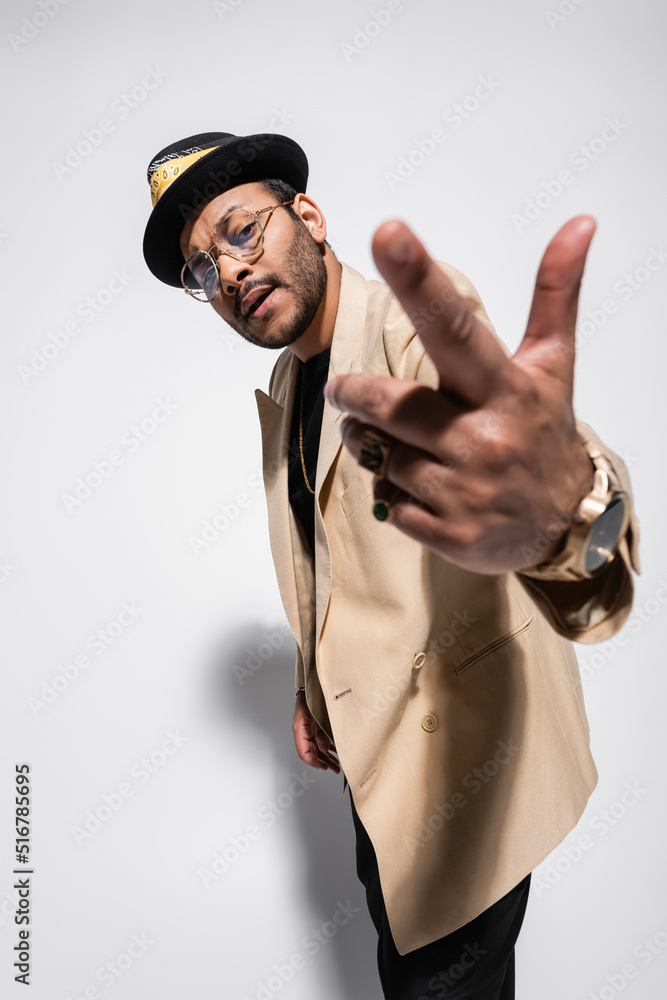 bearded eastern hip hop performer in fedora hat and eyeglasses gesturing on grey. bearded eastern hip hop performer in fedora hat and eyeglasses gesturing on grey.