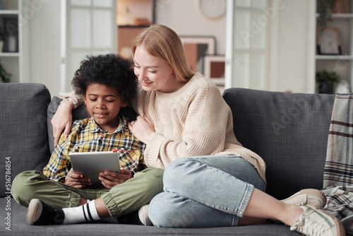 Cuadro en lienzo African little boy playing game on digital tablet while sitting on sofa together