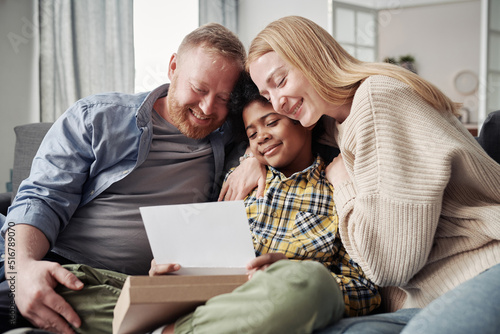 Happy parents embracing their African adoptive son while reading adoption agreement together on sofa photo