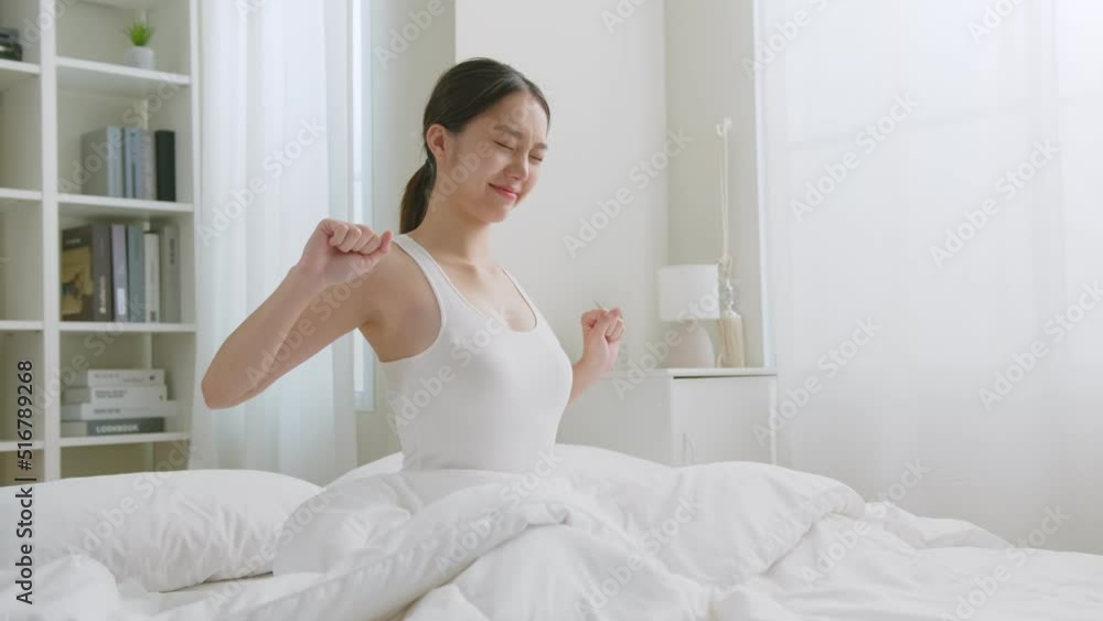 Asian woman wake up in the morning, sitting on white bed and stretching, feeling happy and fresh Asian woman wake up in the morning, sitting on white bed and stretching, feeling happy and fresh