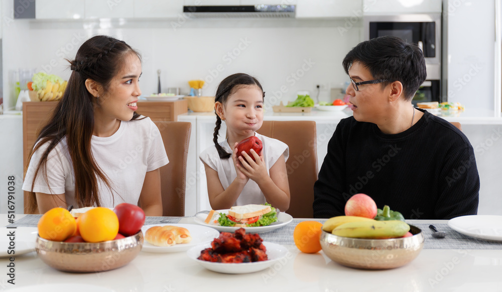 A happy Asian family spends lunch, vegetables, fruit, and dates at the table in their home. Cute little daughter having fun talking. Father, mother