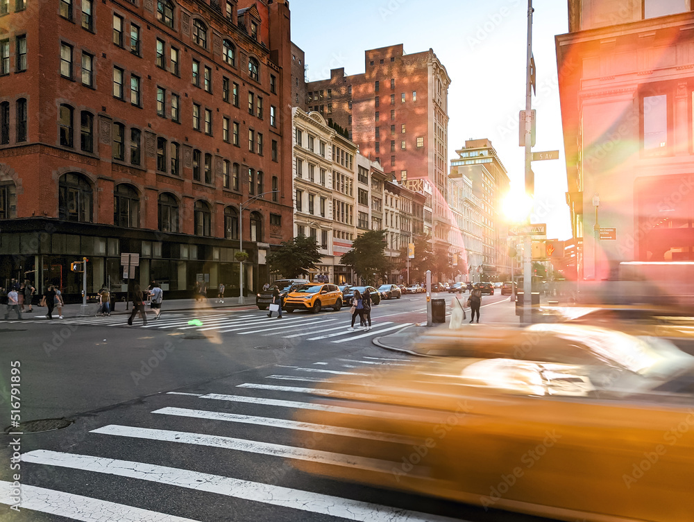 Blurred yellow taxis driving through the intersection of 23rd Street and 5th Avenue in New York City with sunlight background