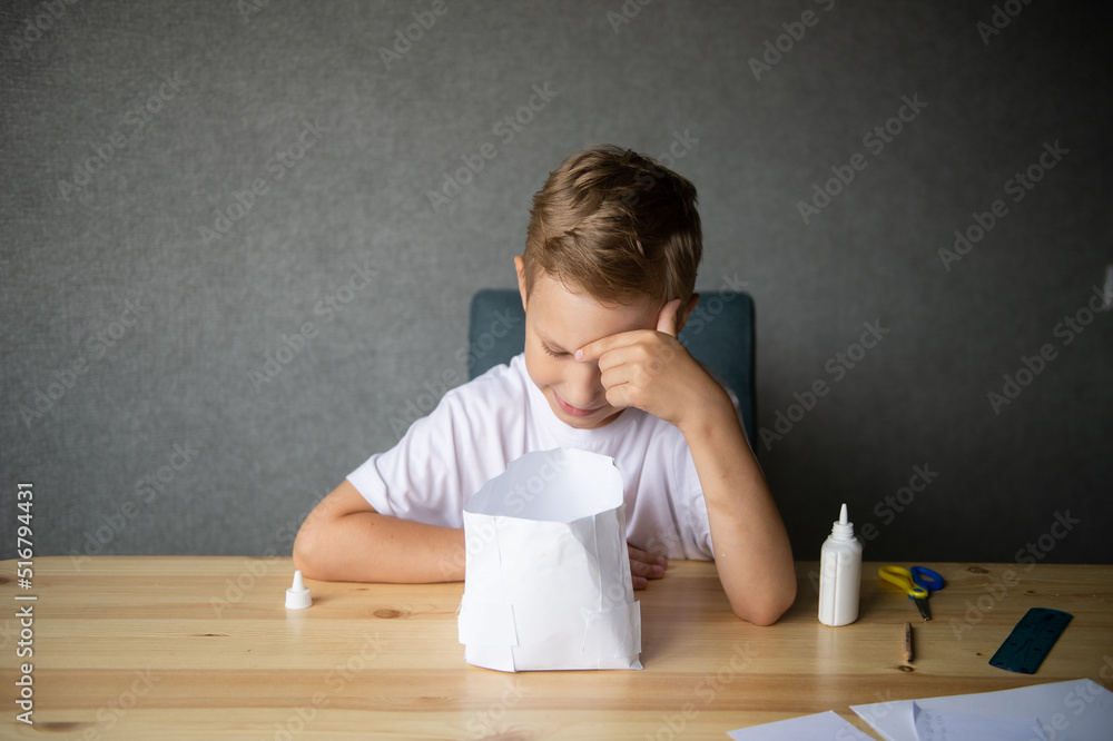 The boy cuts out details from paper. Glue the parts together with glue The boy cuts out details from paper. Glue the parts together with glue