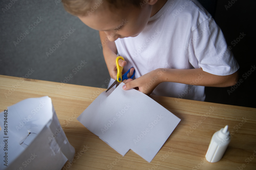 The boy cuts out details from paper. Glue the parts together with glue The boy cuts out details from paper. Glue the parts together with glue