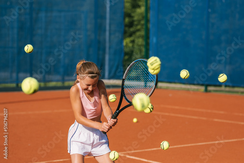 Junior player having fun while training tennis on court. Girl hitting many balls at the same time.