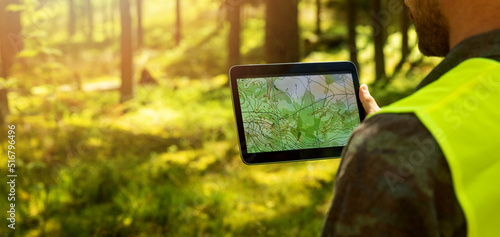 man working with topographic map data on digital tablet in forest. banner with copy space