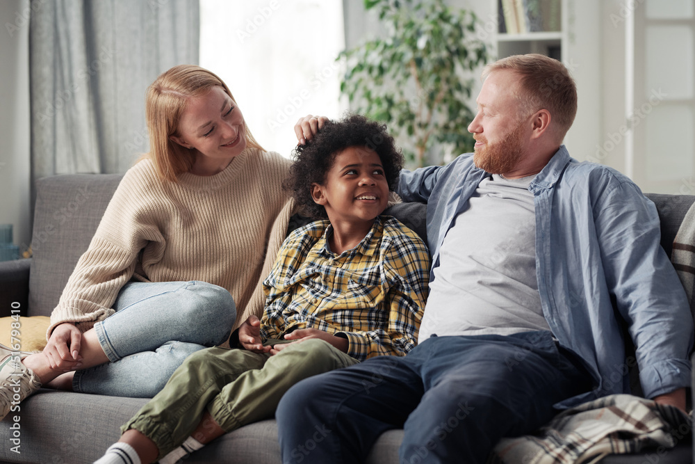 Young parents happy to adopt little boy, they sitting on sofa and talking to each other during their first meeting at home Young parents happy to adopt little boy, they sitting on sofa and talking to each other during their first meeting at home