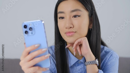 Young Asian girl using modern blue mobile phone with triple camera. Vietnamese person talking on video call on smartphone. BIPOC person lifestyle video clip photo