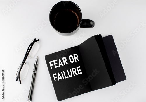 FEAR OF FAILURE written text in small black notebook with coffee , pen and glasess on white background. Black-white style