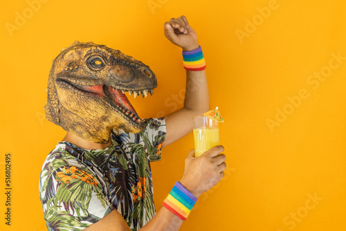 Man in dinosaur animal mask drinking cocktail and dancing wearing LGBTQ pride rainbow wristband,isolated on orange background
