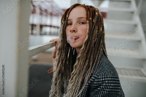 Fotografija Portrait of a freckled teenager girl with dreads making a gum bubble