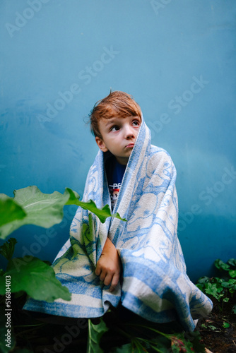 unhappy child boy covered himself with a blanket in the yard