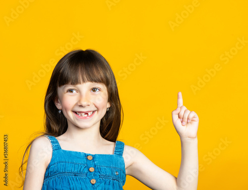A cute little girl smiles a toothless smile with her front tooth falling out, and with her finger up. The tooth fairy will bring a new tooth