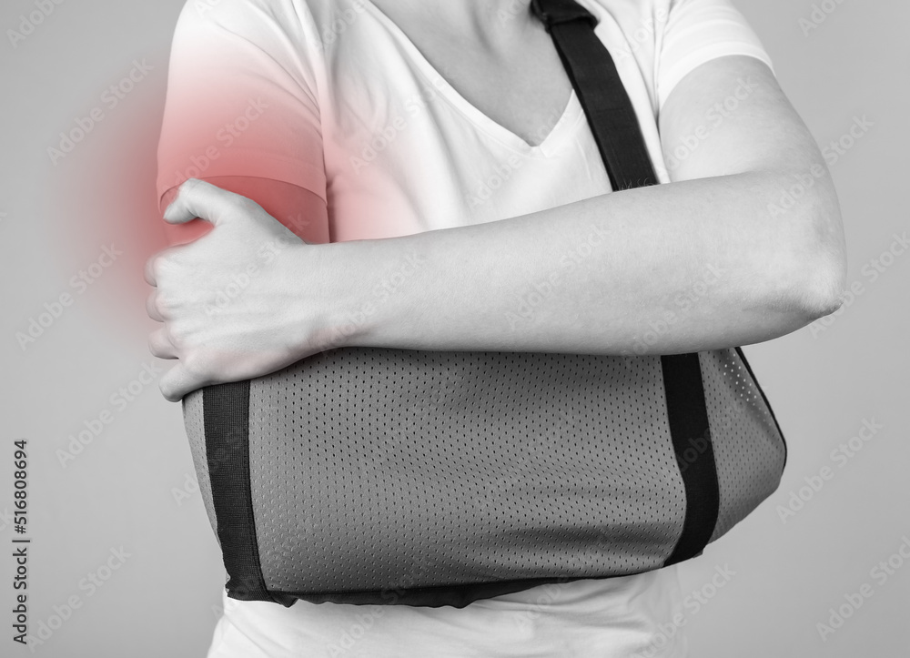 Woman wearing sling to support injured shoulder with red spot. Arm