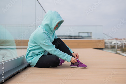Caucasian woman in a hoodie tying her shoelaces before jogging. 