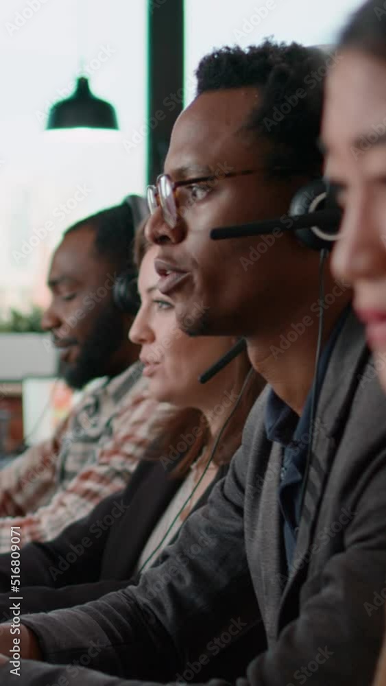 Vertical video: Helpline agents talking to clients on headset at call center job, using computer to have remote conversation. People working at customer service care helping with telemarketing Vertical video: Helpline agents talking to clients on headset at call center job, using computer to have remote conversation. People working at customer service care helping with telemarketing