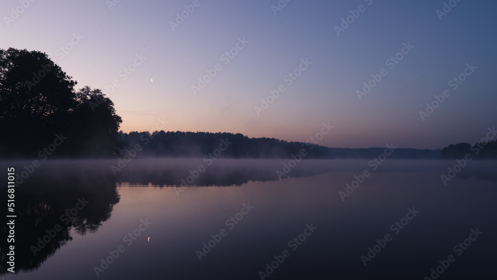 Beautiful mystical landscape. Forest lake at summer night before sunrise. Fog above calm water. Scenic nature.