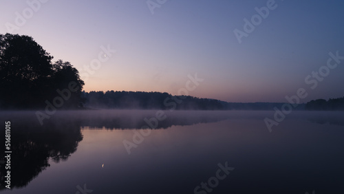 Beautiful mystical landscape. Forest lake at summer night before sunrise. Fog above calm water. Scenic nature. © Anastasia