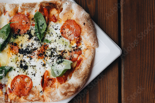 Fresh baked pizza with melted cheese, Italian herbs and tomato sauce and fresh basil on a white plate on a kitchen background, selective focus