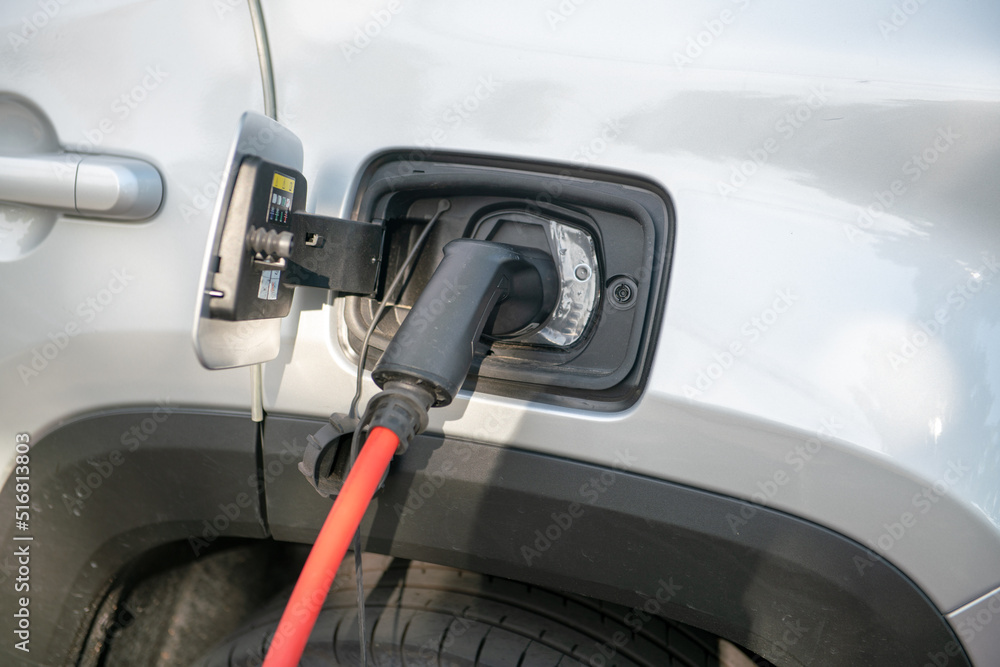 electric car being recharged, connected with the red cable to the electrical control unit, where it draws energy, in a dedicated parking lot. Zero emissions in cities with green ecological policies. electric car being recharged, connected with the red cable to the electrical control unit, where it draws energy, in a dedicated parking lot. Zero emissions in cities with green ecological policies.
