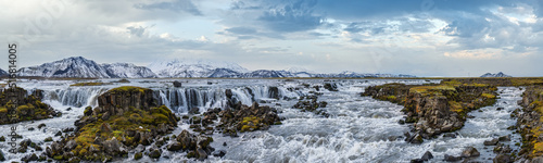 Season changing in southern Highlands of Iceland. Picturesque waterfal Tungnaarfellsfoss panoramic autumn view. Landmannalaugar mountains under snow cover in far.