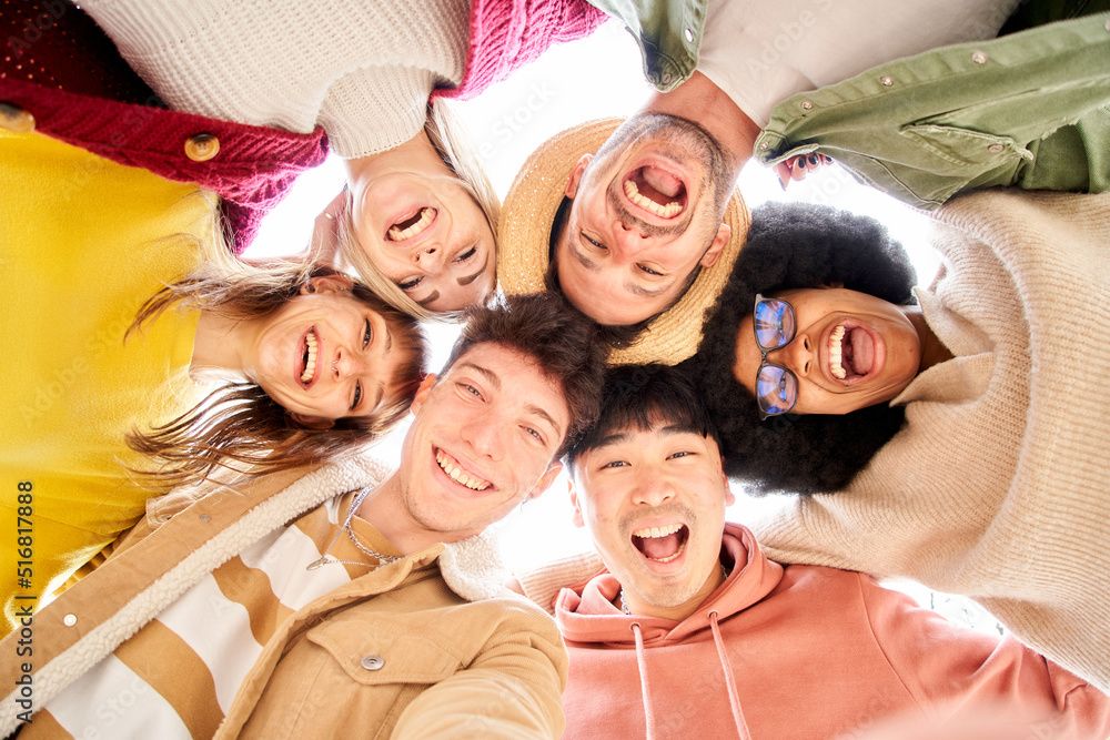 Low angle of group of cheerful young friends in circle taking selfie portrait. Happy people looking at the camera smiling. Concept of community, youth lifestyle and friendship