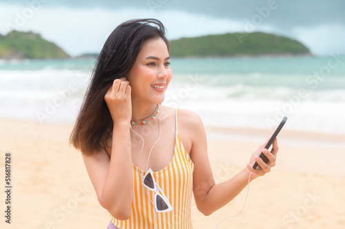 Young Beautiful woman in Bikini listening to music and using smartphone on the beach, Summer, vacation, holidays, Lifestyles concept.