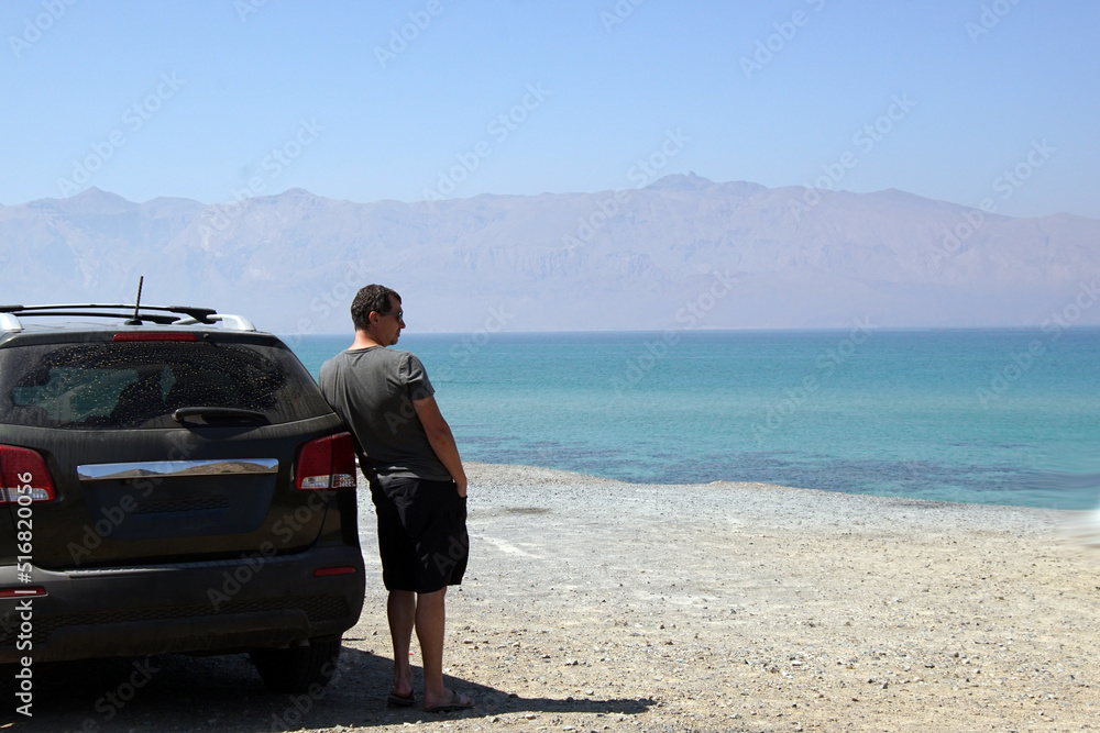 Lonely man stands near car parked at the blue sea.
